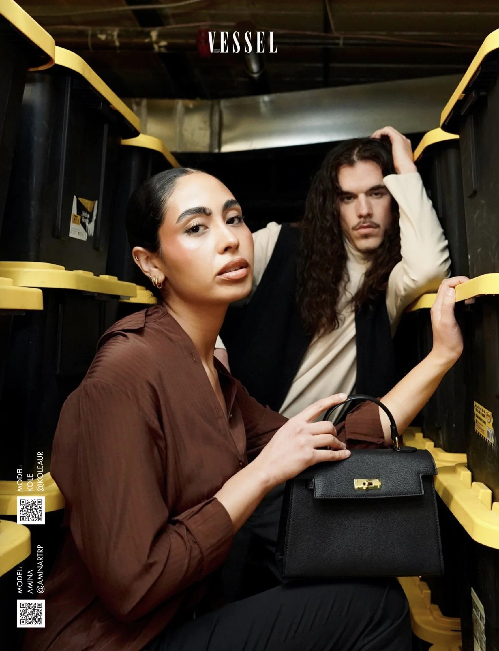 Two young women with dark hair pose in a store aisle with yellow shelving. The woman in the foreground has her hair tied back and wears a brown shirt, holding a black handbag. The woman behind her has long, wavy hair and wears a cream-colored top, with her hand on her head. The photo has the text 'VESSEL' at the top.