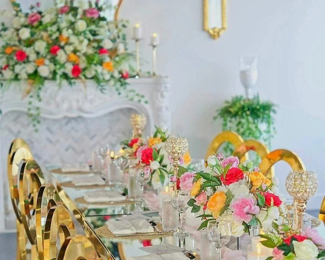 Elegant dining table set for a celebration with colorful floral centerpieces, gold chairs, and candle holders in a decorated room.