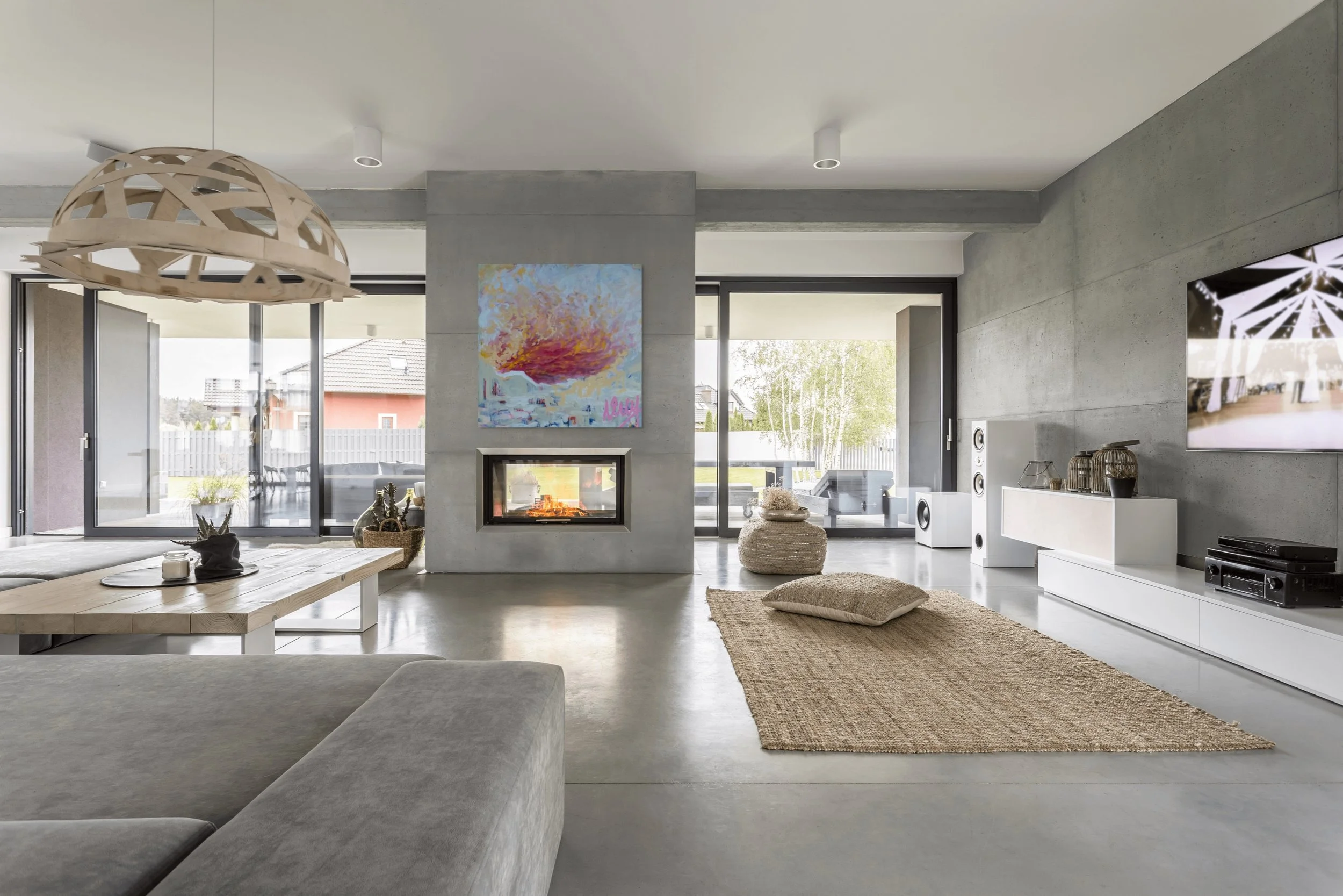 Modern living room with concrete floors, a fireplace, large glass sliding doors, a beige rug, and contemporary furniture.