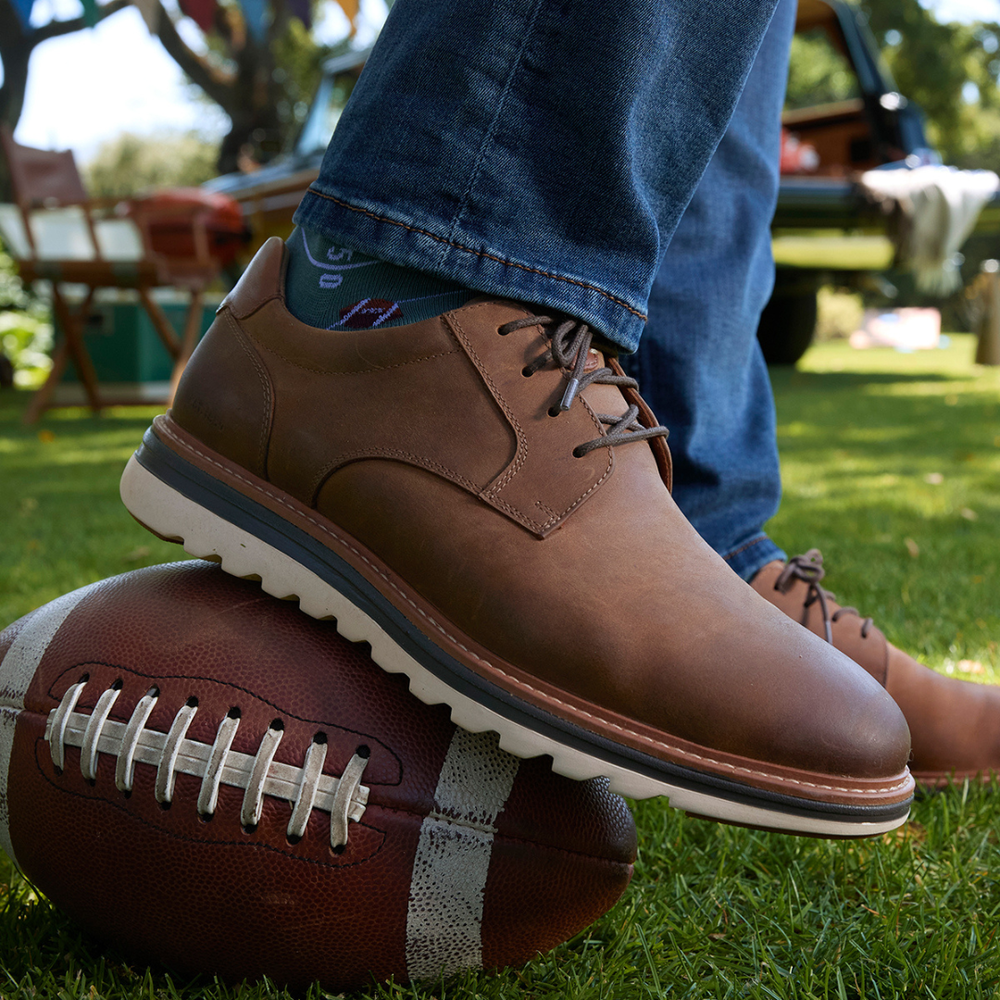 Brown leather lace-up shoe resting on a football on the grass