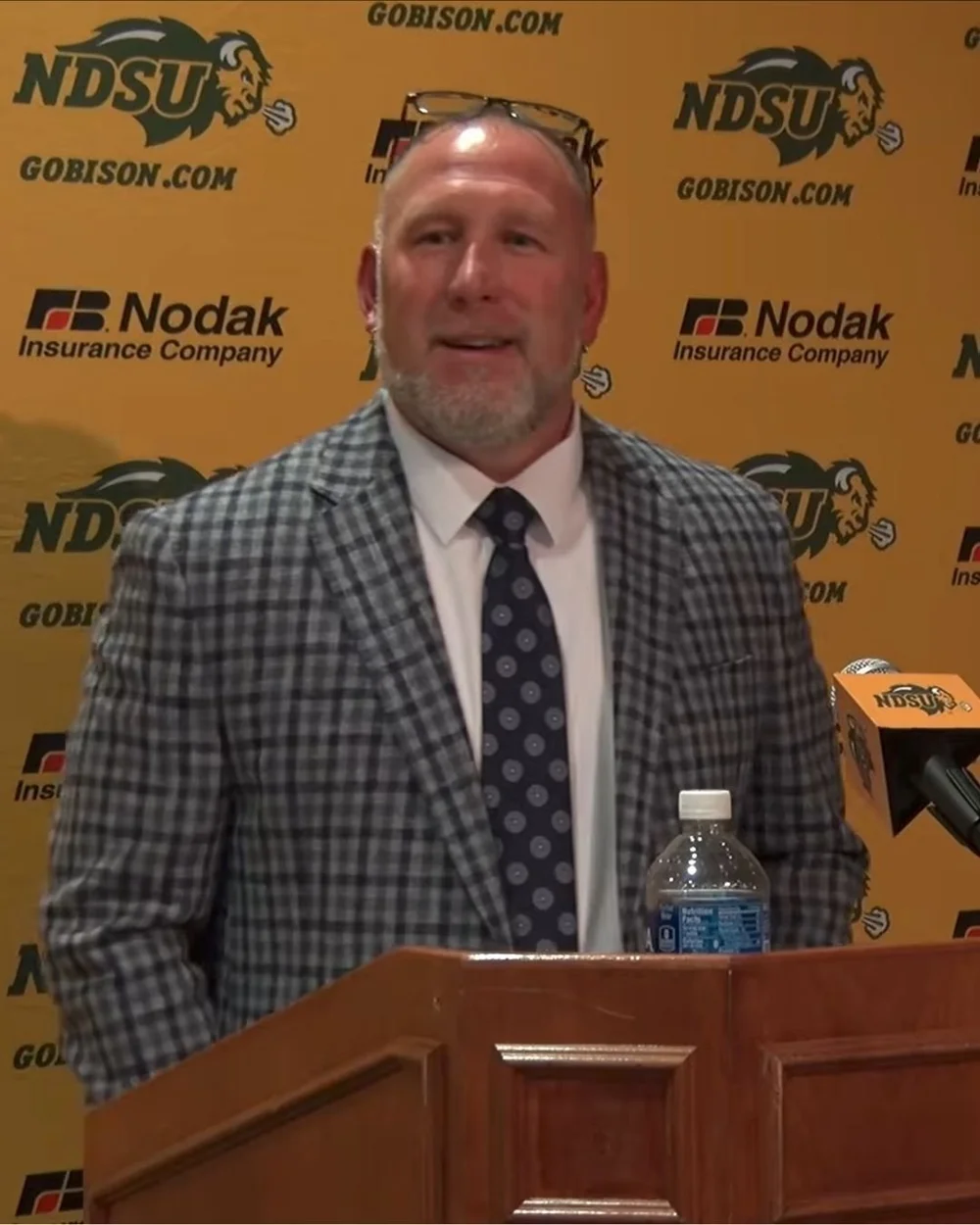 Speaker in a plaid sport coat at an NDSU Athletics press conference podium