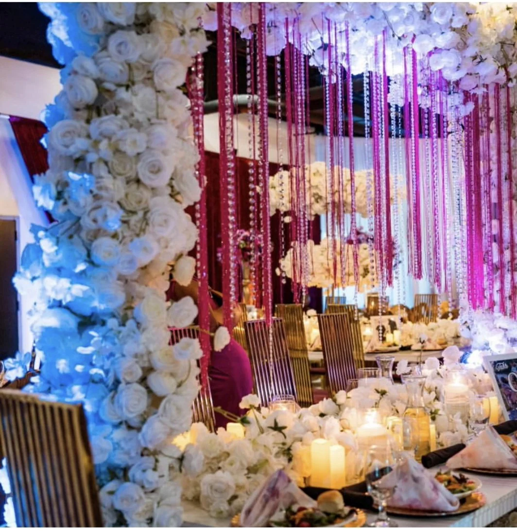 Wedding banquet table decorated with white flowers, candles, and pink hanging ribbons or drapes. Elegant chairs and place settings. Decor styled by vendor TP Collective.
