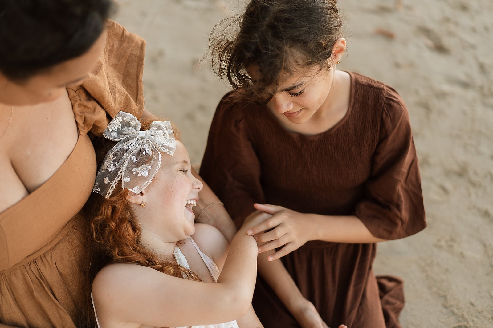 Three women are laughing and smiling together, with one young girl lying down and holding hands with one of the women, on a Kewarra Beach.