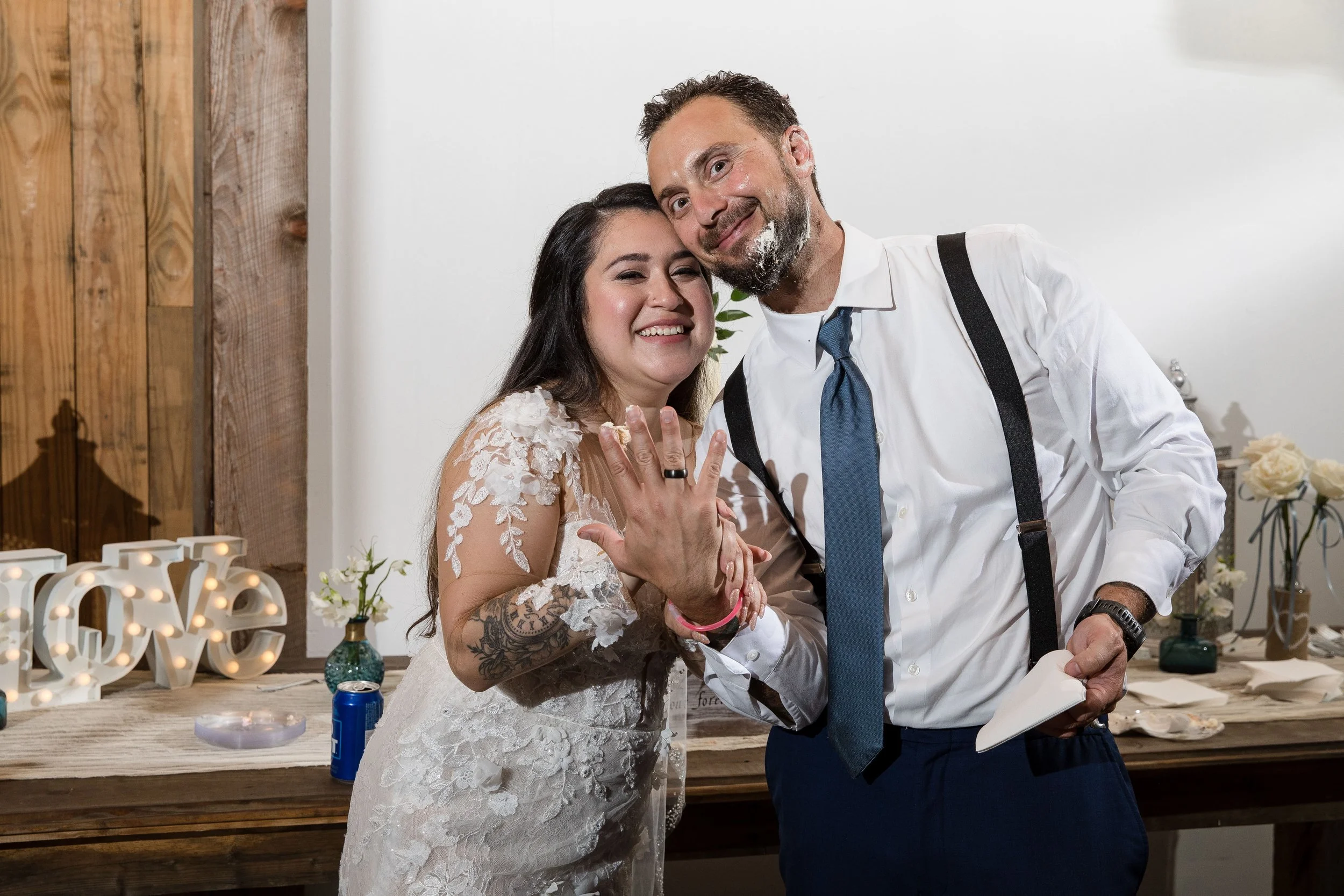 A newlywed couple smiling and showing off their wedding rings at a wedding reception or celebration.