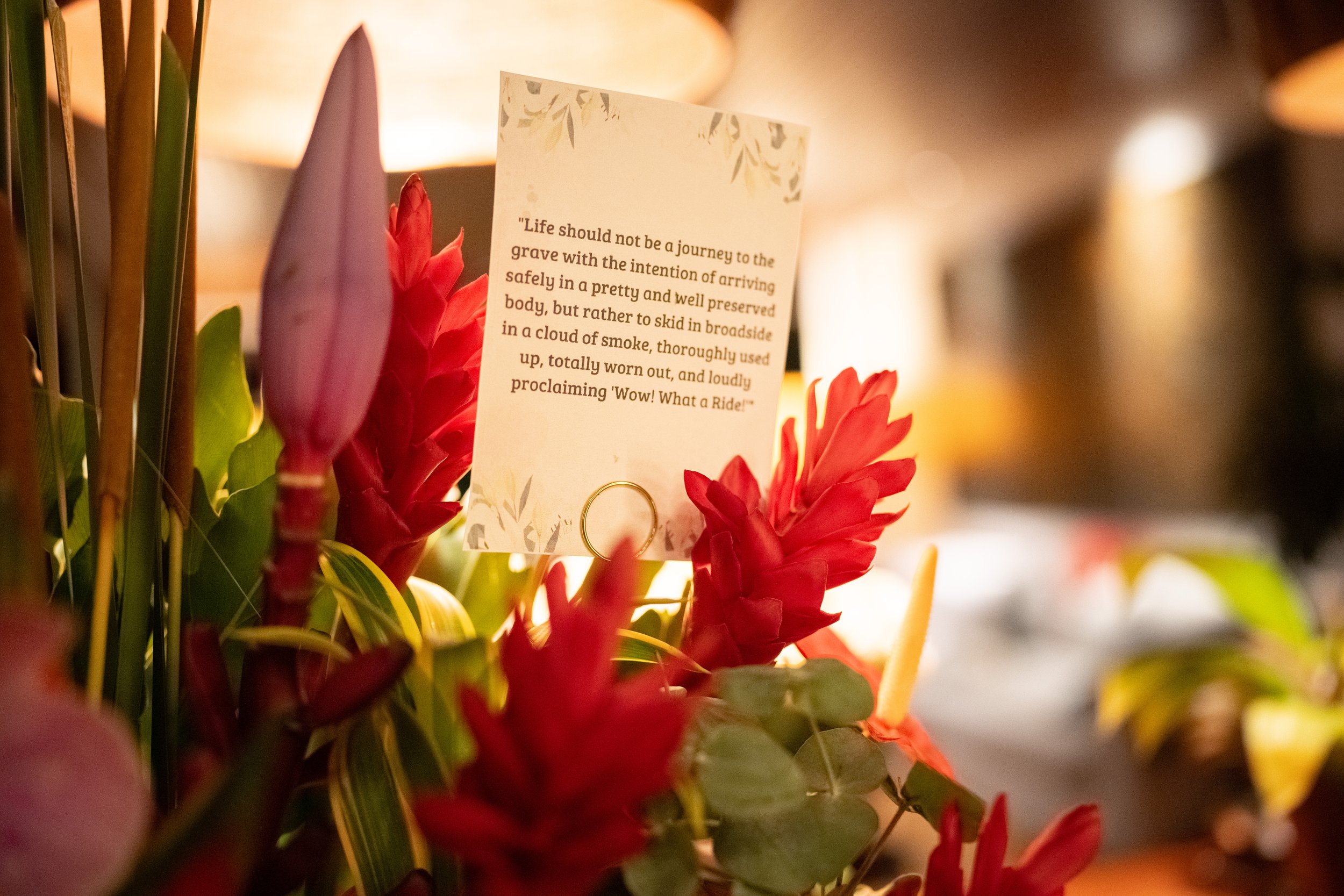 Close-up of a flower arrangement with a card containing an inspirational quote, surrounded by greenery and vibrant red flowers. High-end retreat center in Pejeng, Ubud, Bali