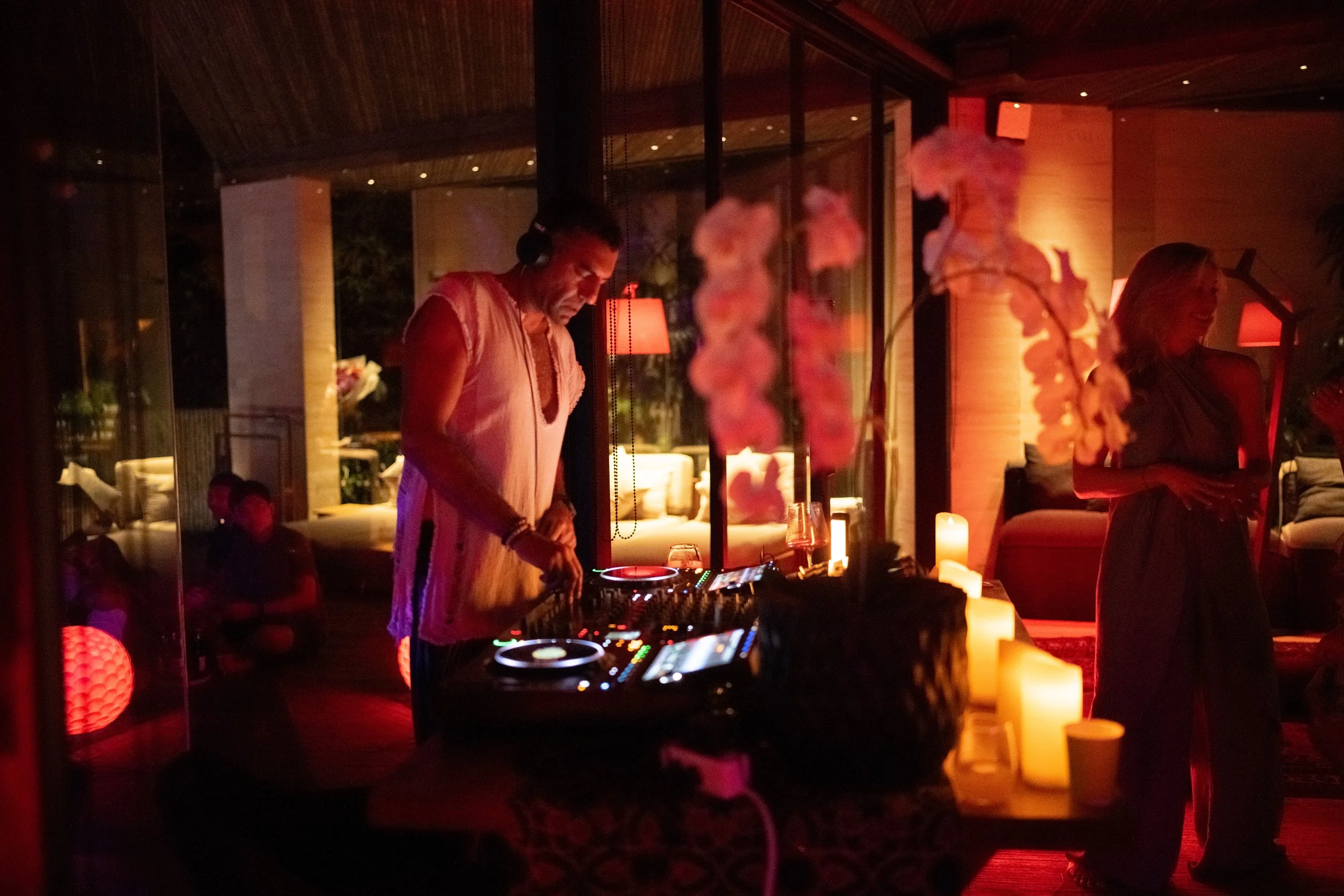 A man is DJing at a dimly lit indoor party with candles and people socializing, likely in the evening.High-end retreat center in Pejeng, Ubud, Bali