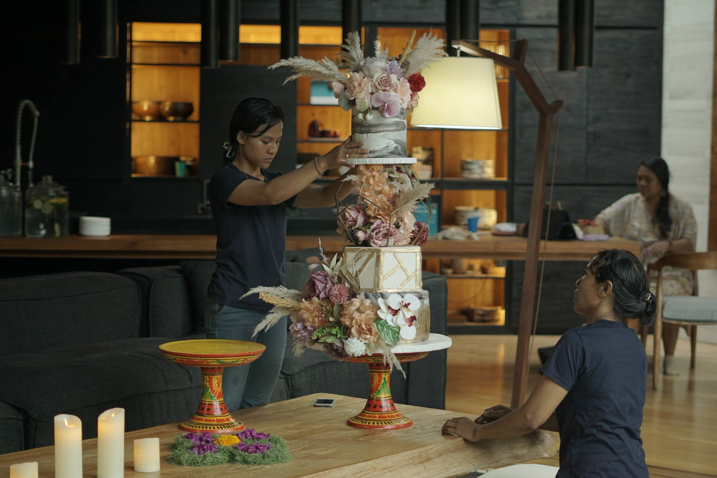 Elegant floral arrangement with pink, purple, and red flowers in a marbled vase, placed on a geometric gold stand with a blurred background of warm lighting and wooden interior.High-end retreat center in Pejeng, Ubud, Bali