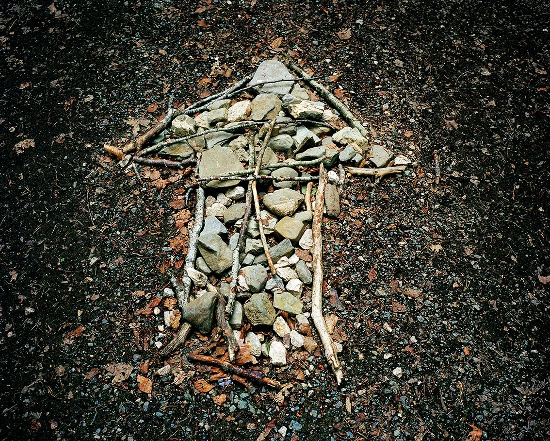 Diamond shape created with stones, branches and dead leaves on black, earthy ground.