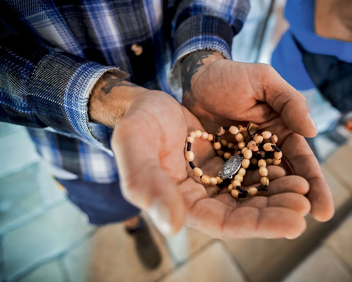 Hands of a man holding a wooden rosary with a religious medal.