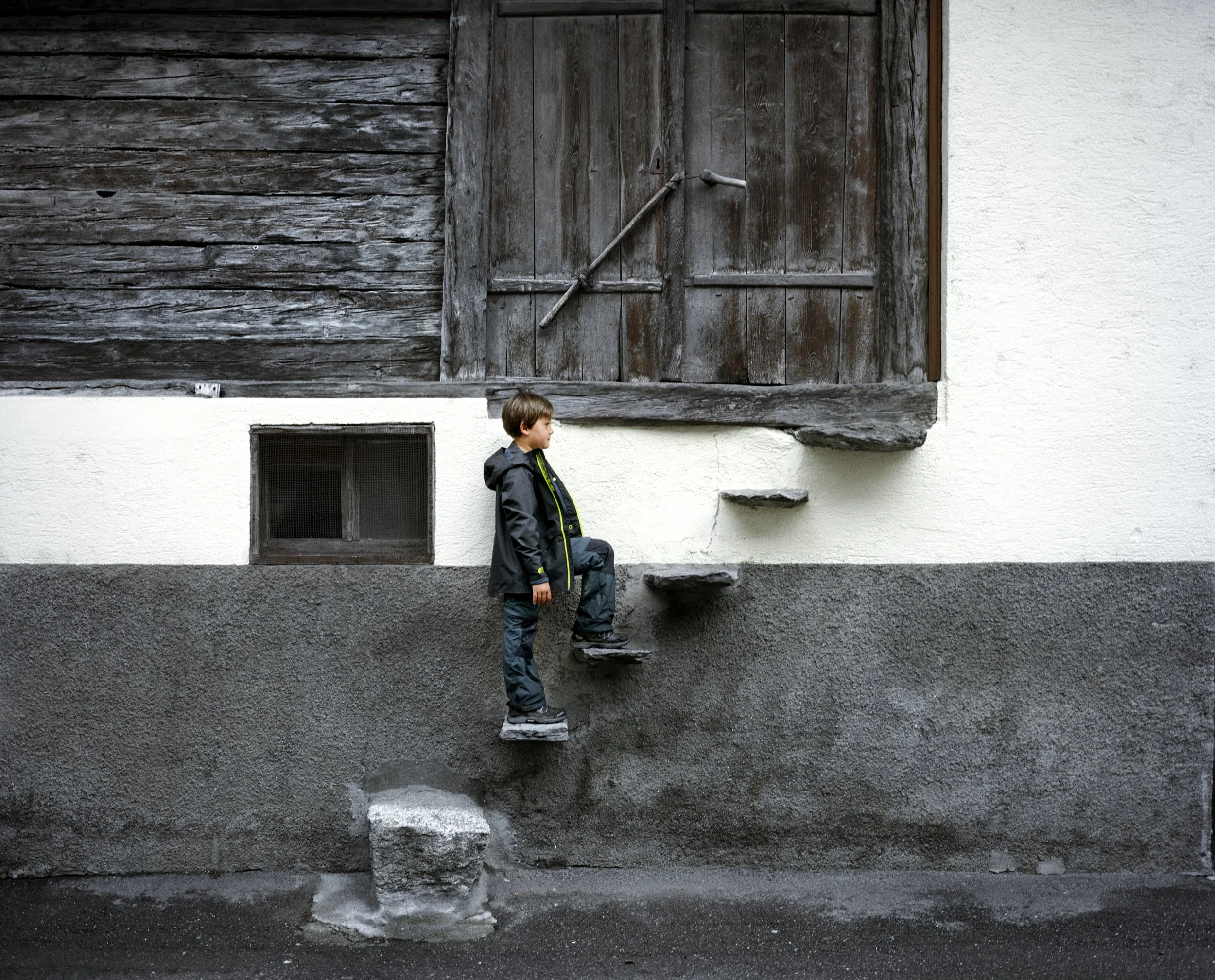 Young boy walking on steps hung against a front wall.