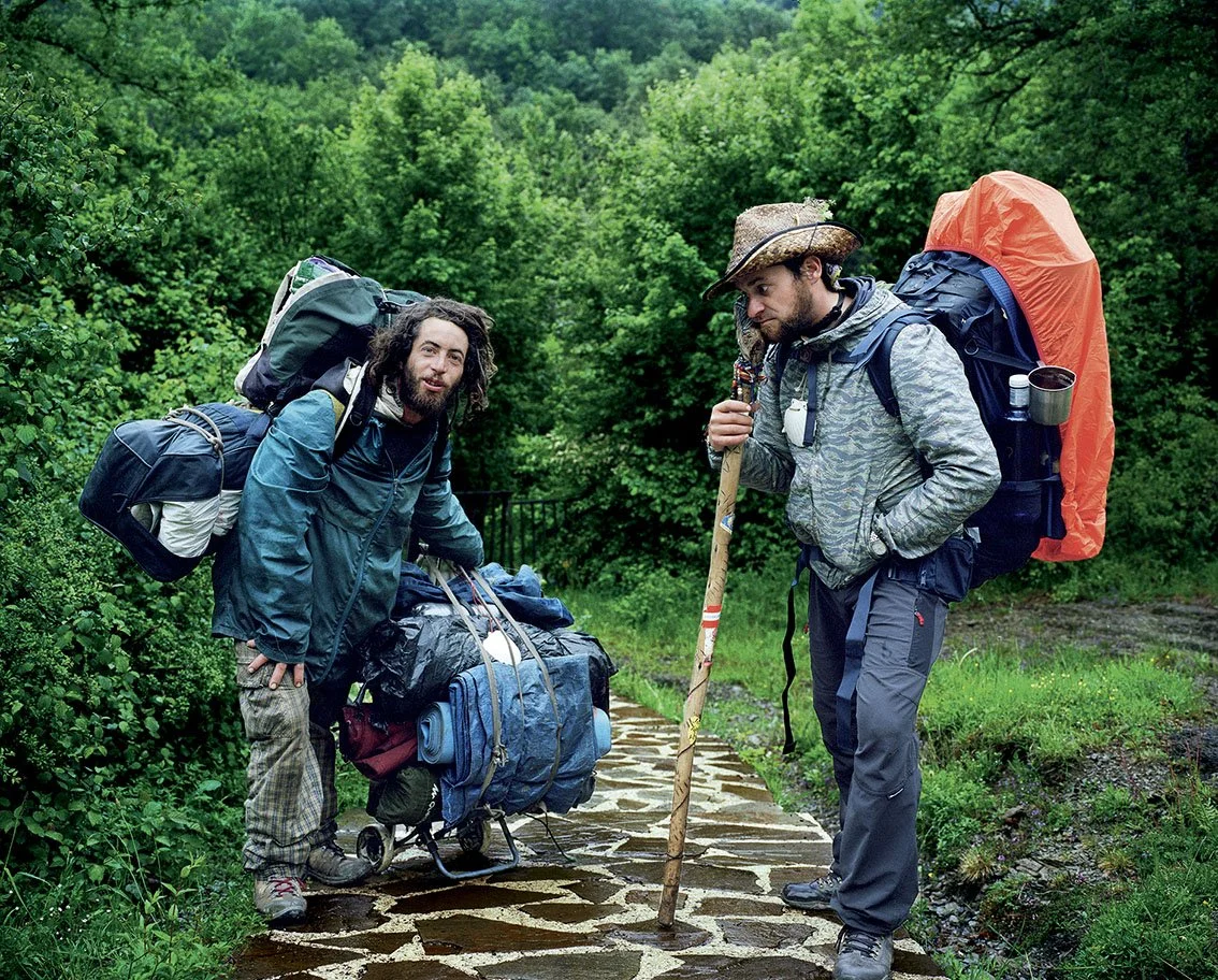 Two hikers with heavy backpacks on a forest trail.