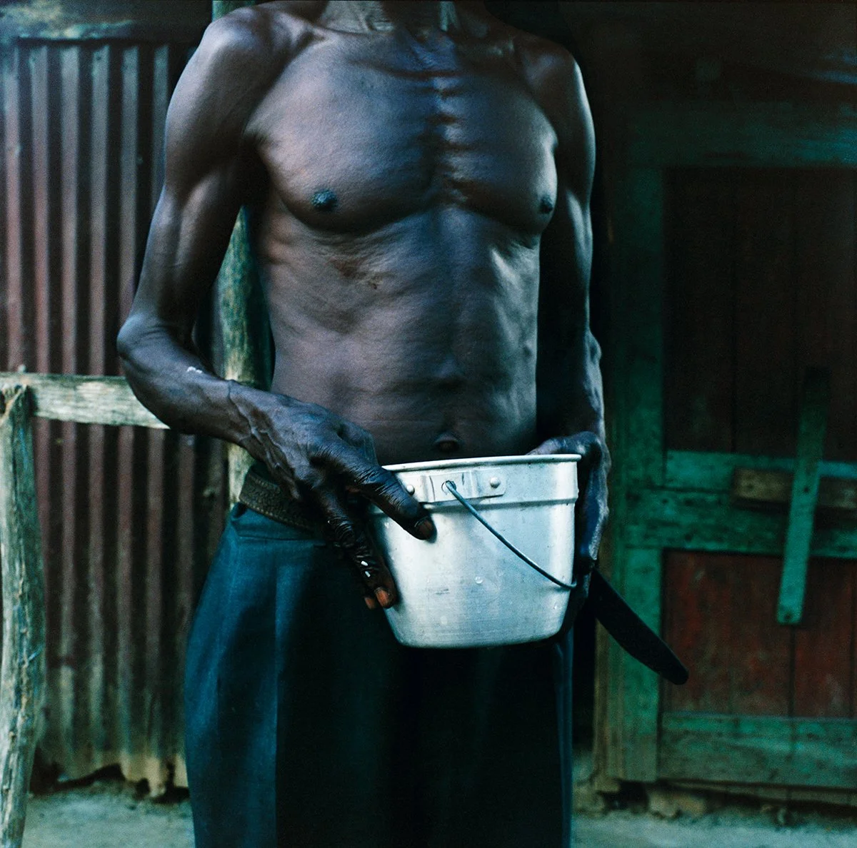 Shirtless man holding a metal bucket on a farm