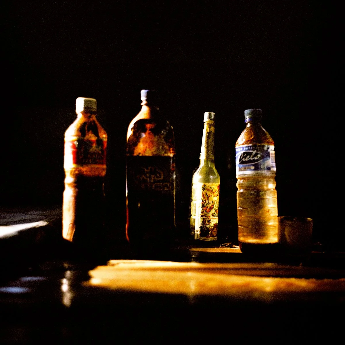 Four glass bottles, two water and two drinks, on a table in the dark.