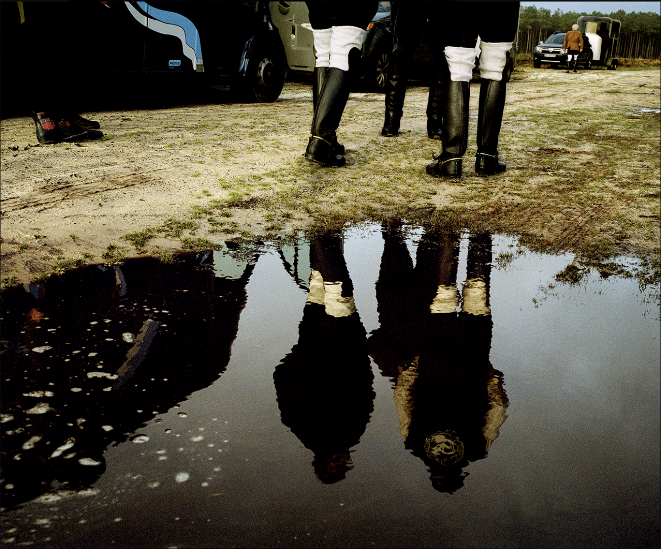 Groupe de cavaliers en bottes, vue de derrière, reflet dans une flaque d'eau, en pleine campagne.