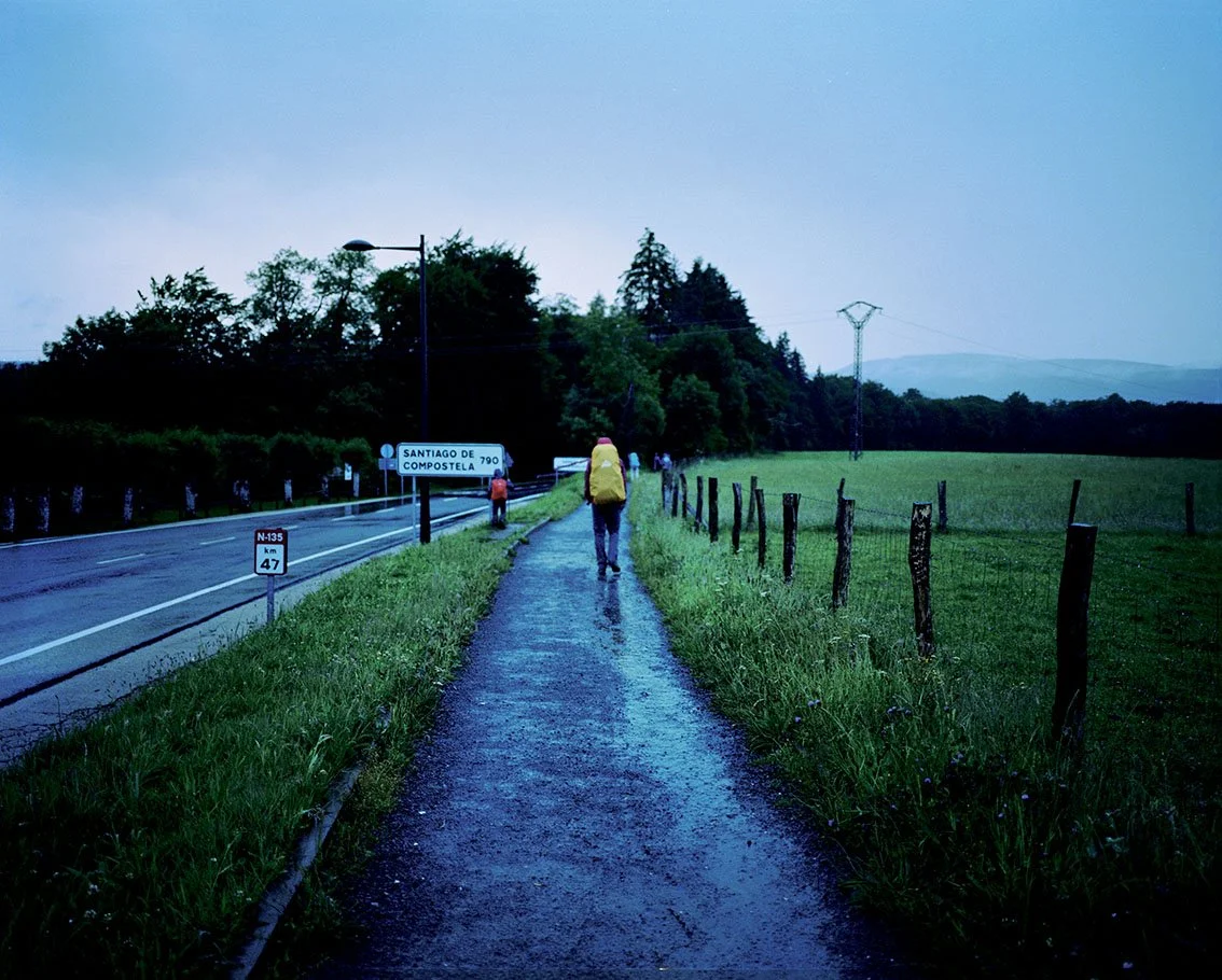 Dirt track alongside a road with hikers carrying backpacks, heading for Santiago de Compostela.