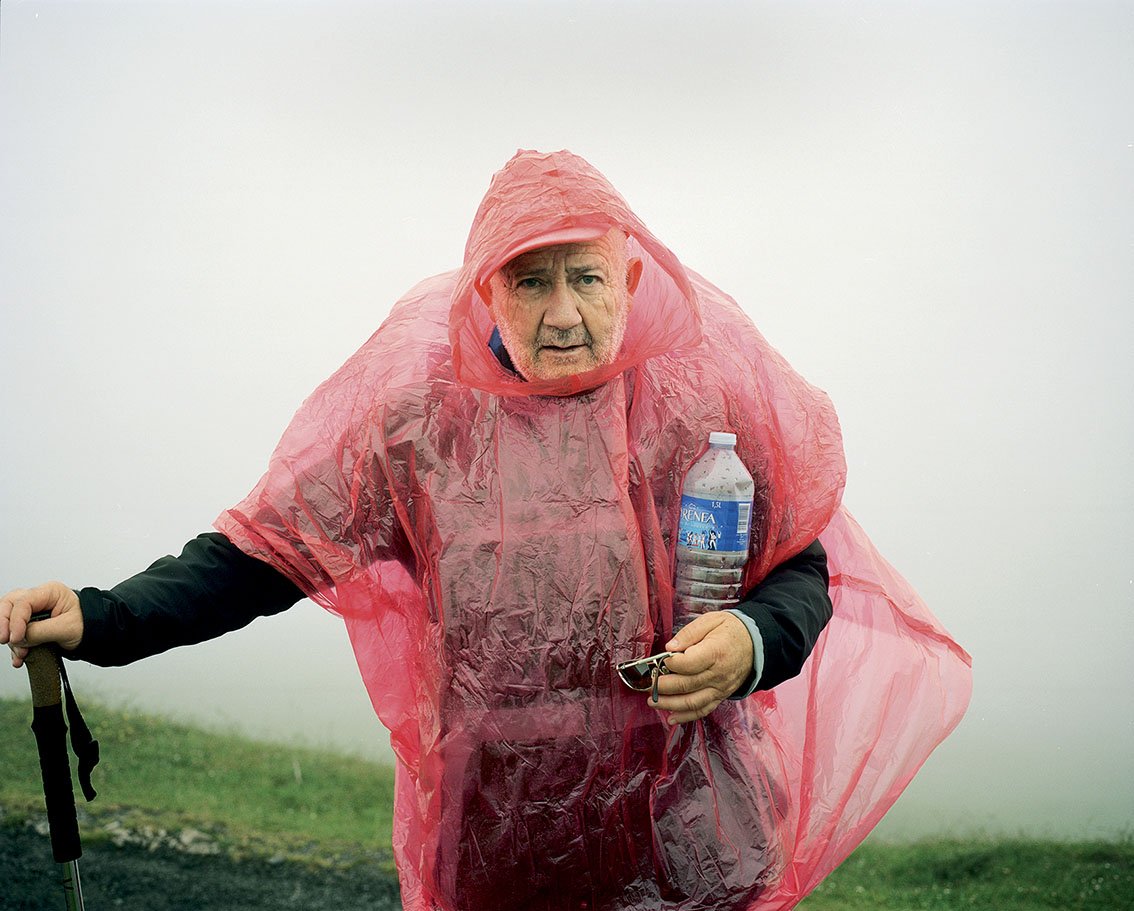 A man wears a pink plastic poncho, holding a bottle of water, in a foggy environment.