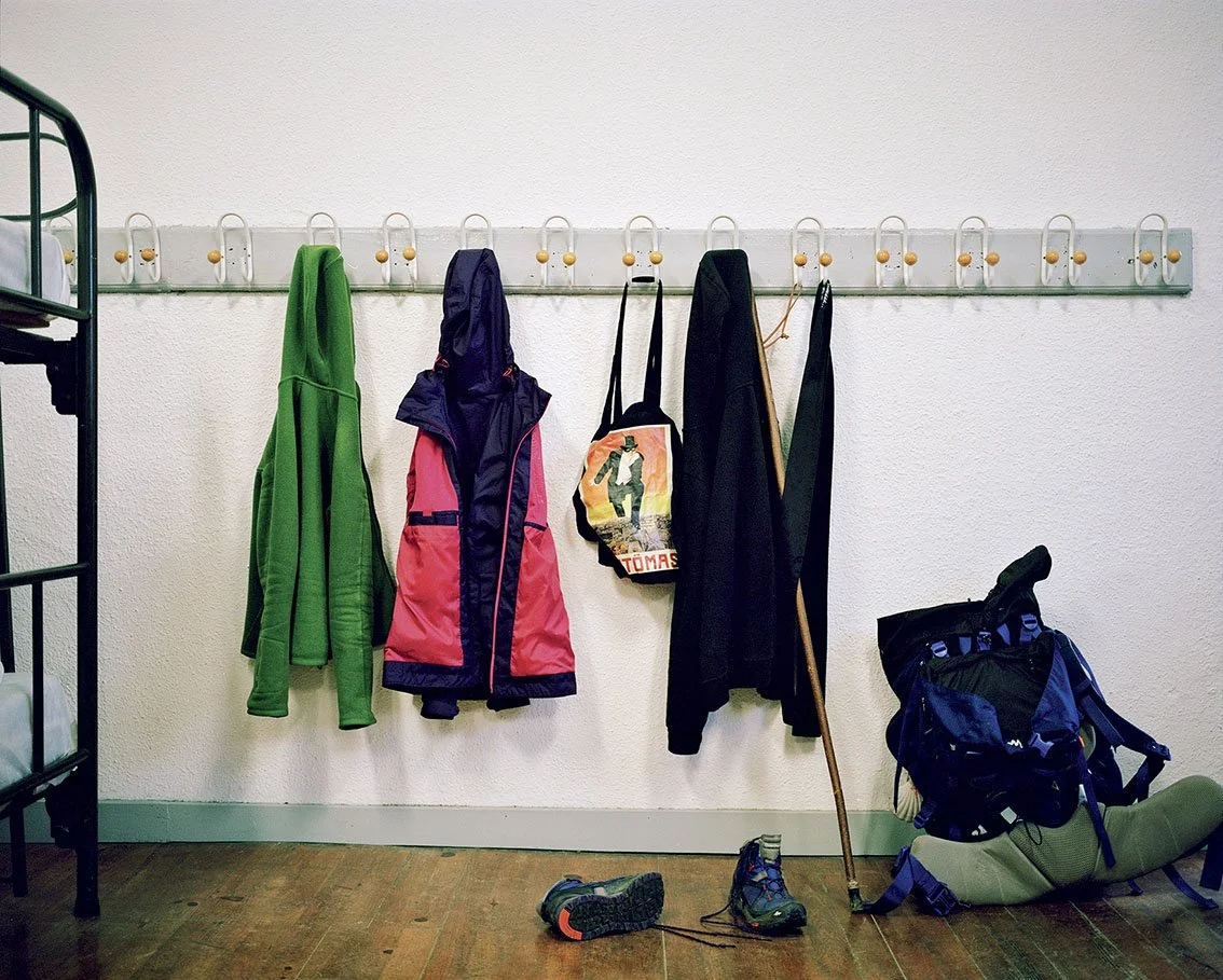 Clothes and rucksack hung in an entrance or changing room, with shoes and walking sticks on the floor.