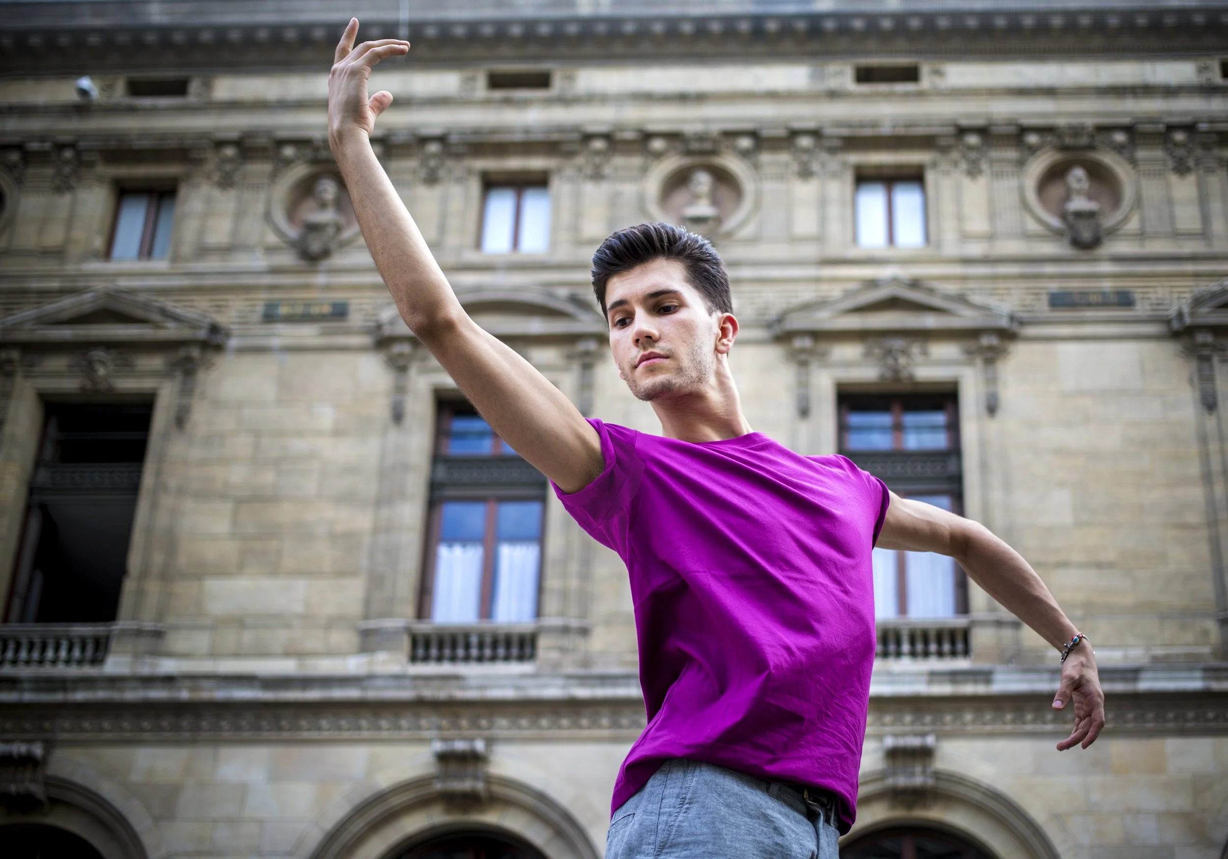 Young man performing a dance or gymnastic pose in front of an old building with carved windows and decorations.
