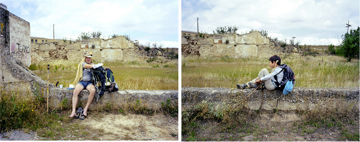 Two people sitting on a stone ledge in a natural outdoor setting with grasses and ruined buildings, each carrying a backpack, with a casual style and a hiking or travel vibe.