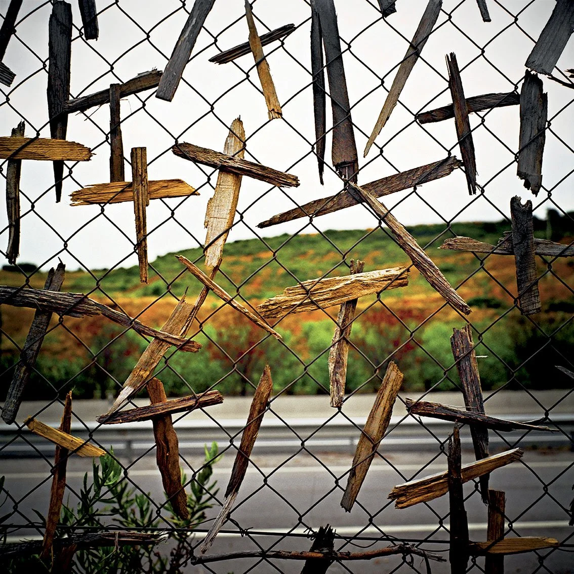 Wire fence with broken pieces of wood, green hill and road in background