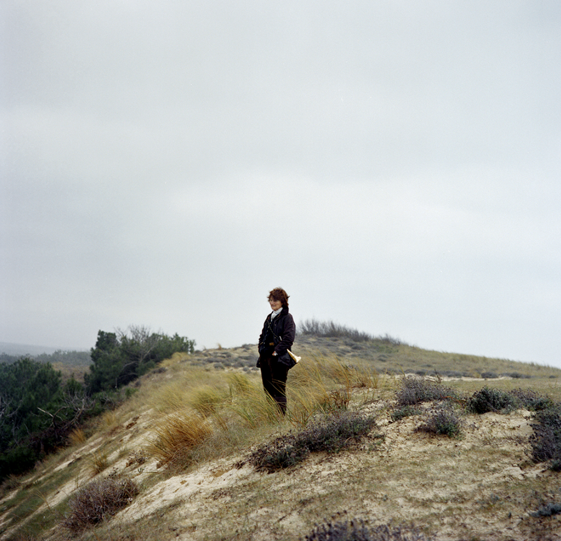Une femme debout sur une colline herbeuse, regardant vers l'horizon sous un ciel nuageux.