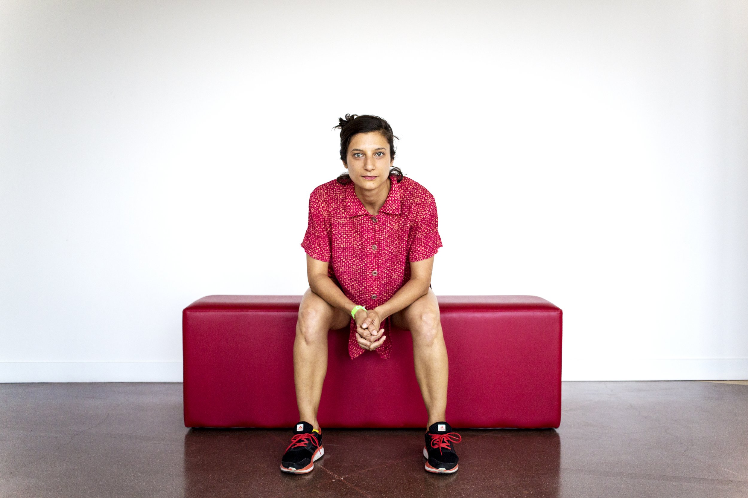 Young woman sitting on a red bench in casual dress, in a white room