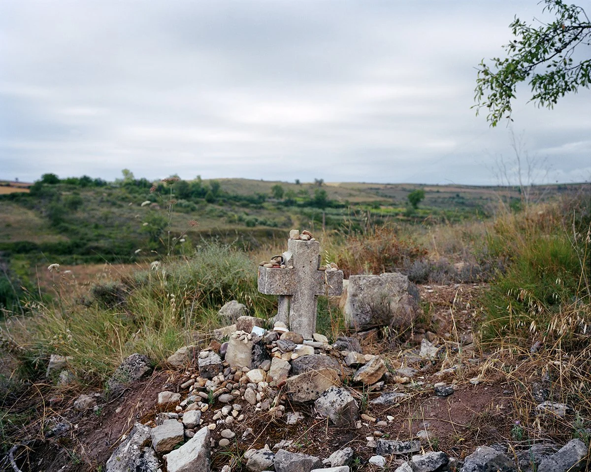 Abandoned stone cross in a rural landscape with grass and hills in the background.