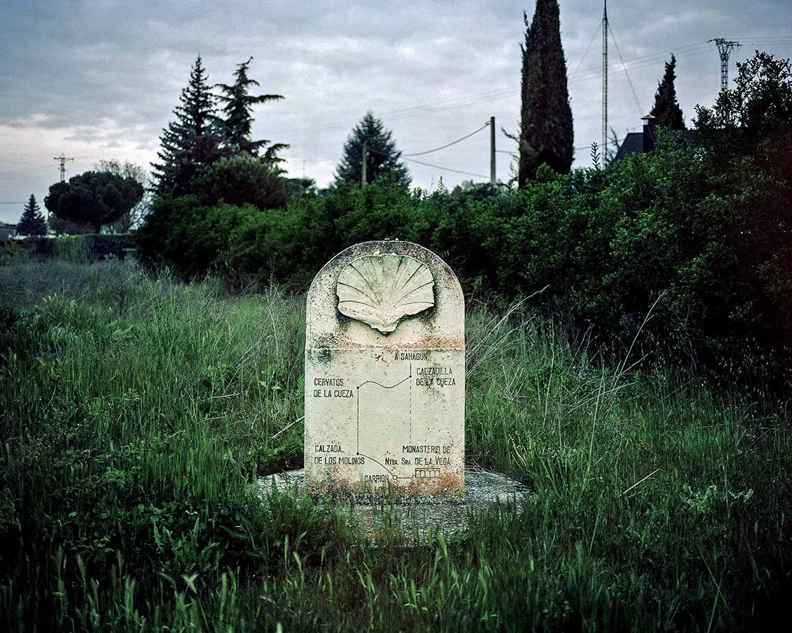 A stone milestone in a grassy field with trees and a cloudy sky in the background.