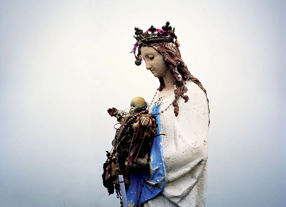 Statue of a woman with a crown, holding a baby, decorated with jewels and colorful accessories, against a dark gray sky.