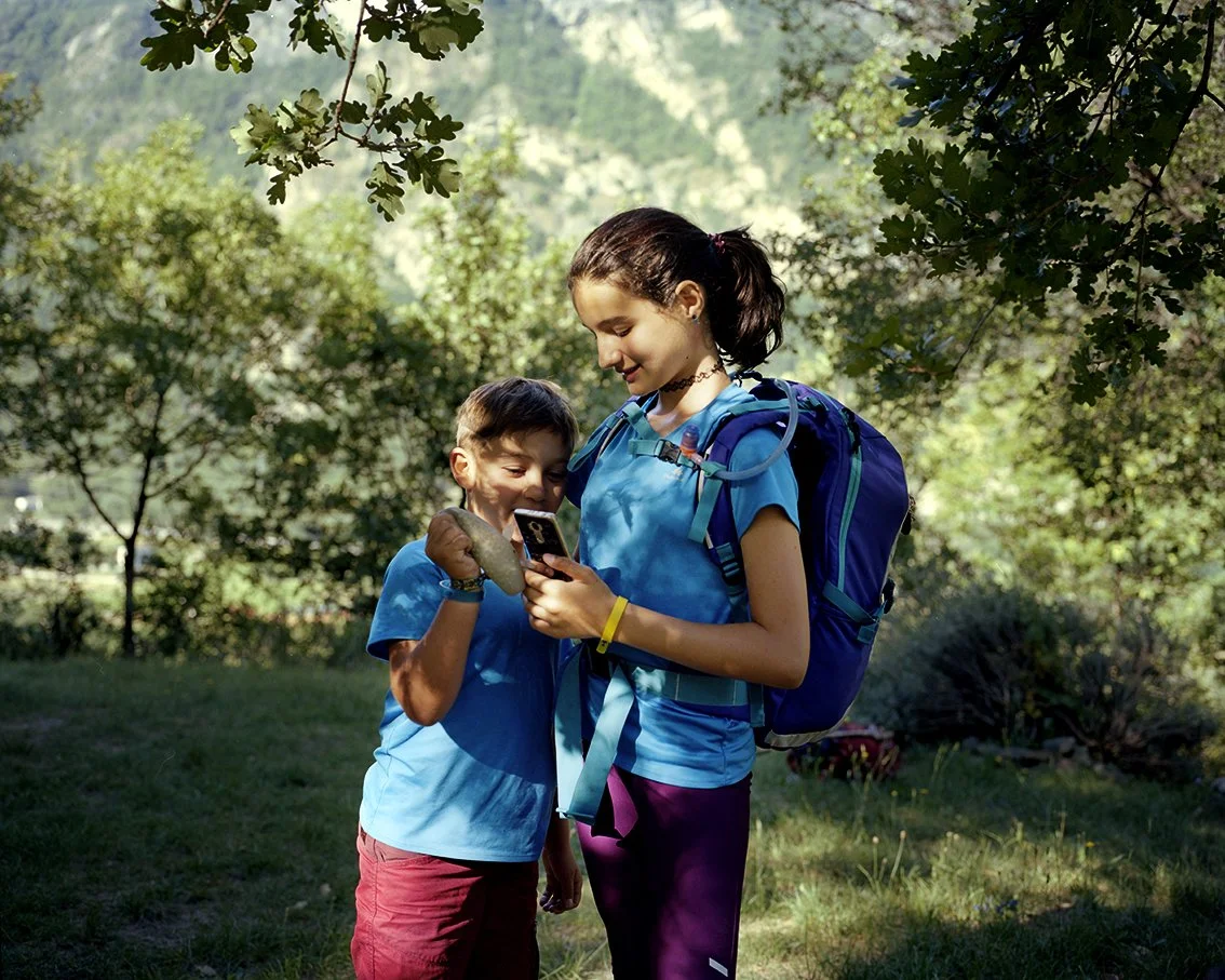 A girl and a boy in hiking clothes, looking at a cell phone in a forest park.