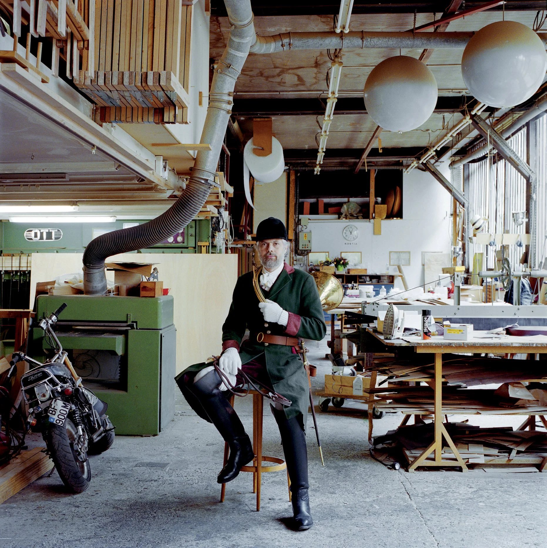 A man disguised as a historical soldier poses in a workshop filled with tools, plans and work materials.