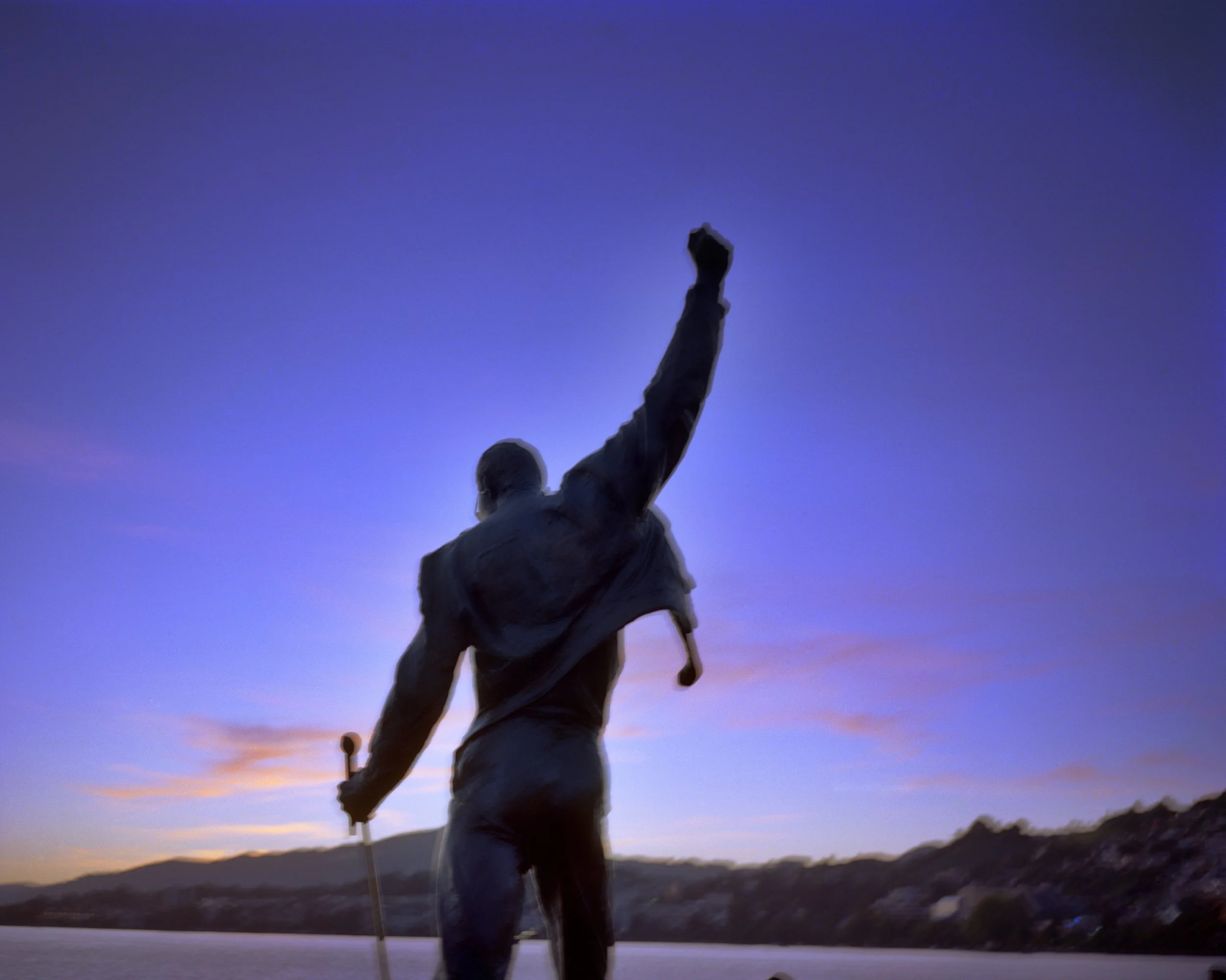 Statue of Nelson Mandela with one arm raised, silhouetted against a blue and purple twilight sky.