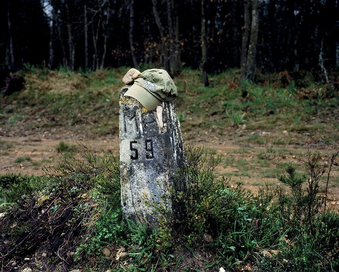 Stone boundary marker with military hat on top, located in a wooded area.
