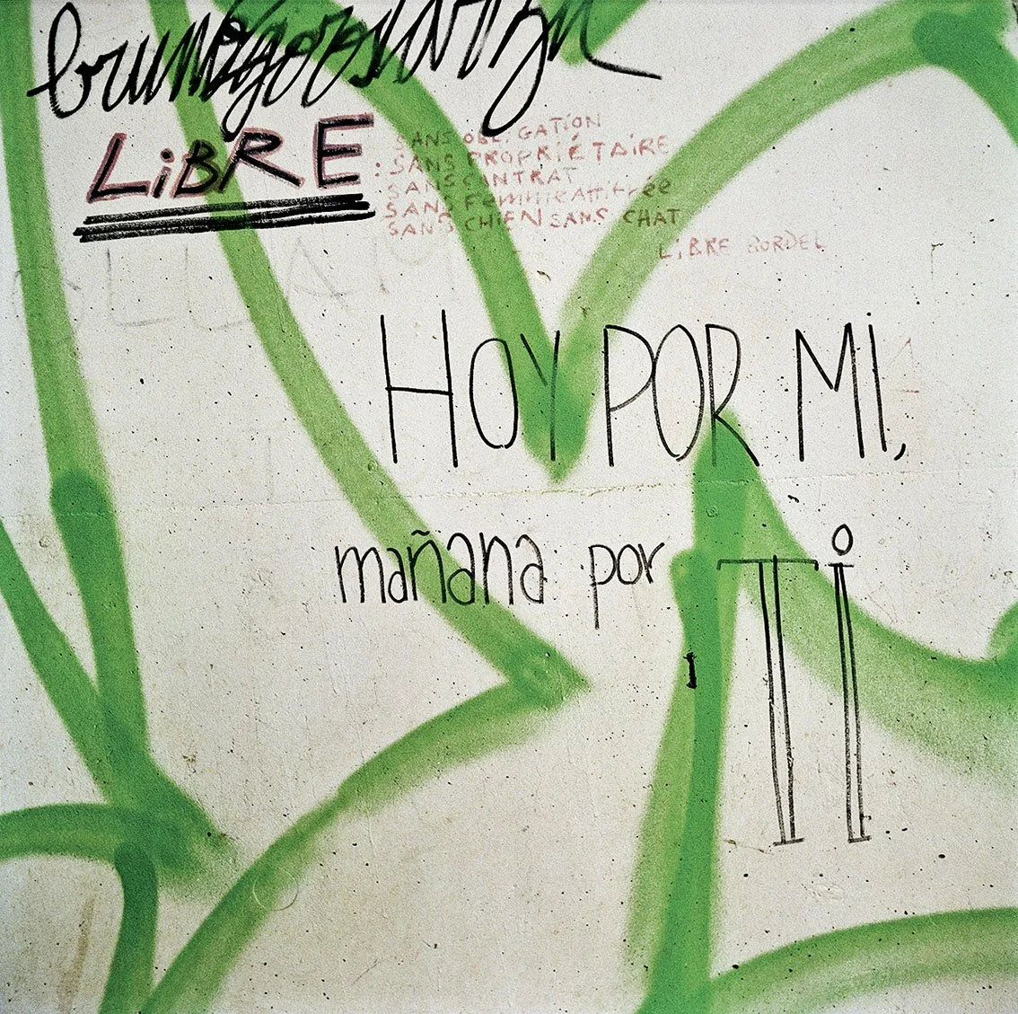 Graffiti on a wall with inscriptions in French, including "Comment j'aime" and "maman pour tipi". Green graffiti damage in background.