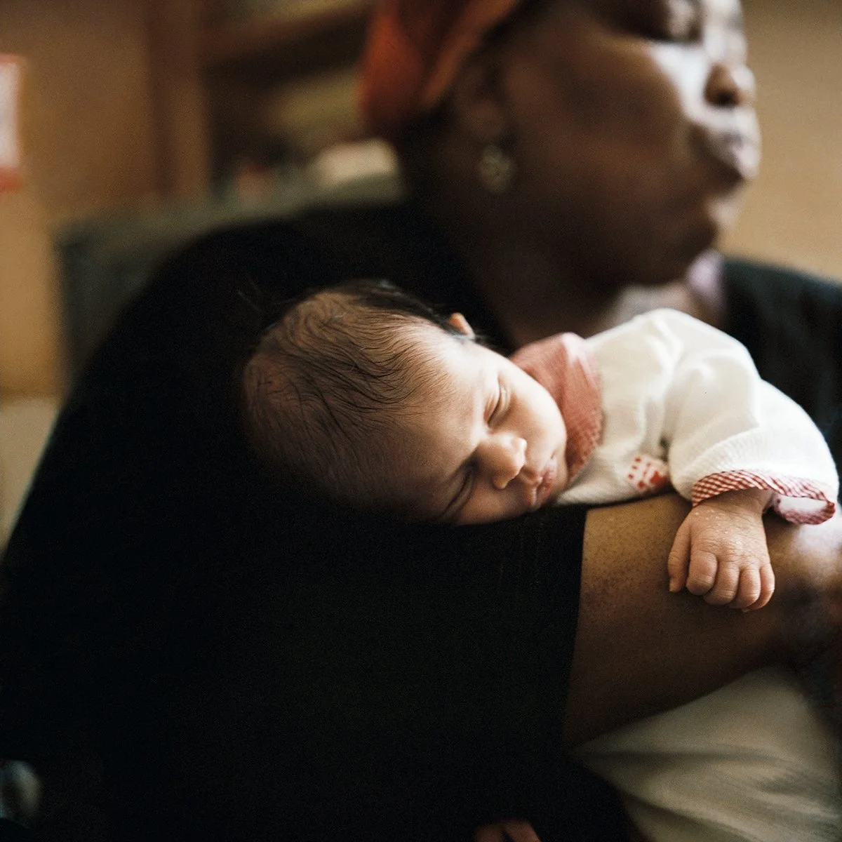Un bébé endormi dans les bras d'une femme, probablement sa mère, dans un intérieur chaleureux.