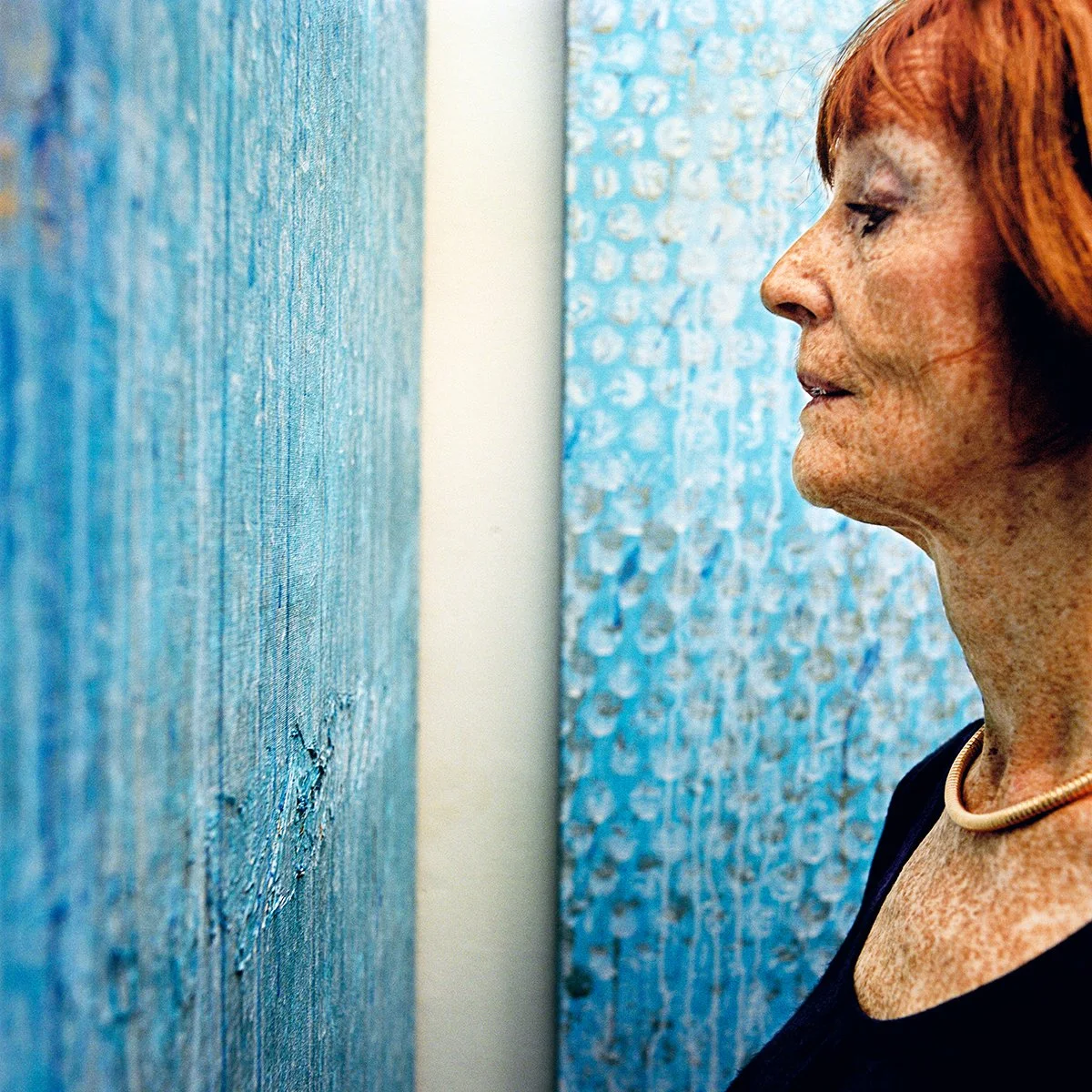 A woman with red hair, attentively observing a blue work of art in a gallery.