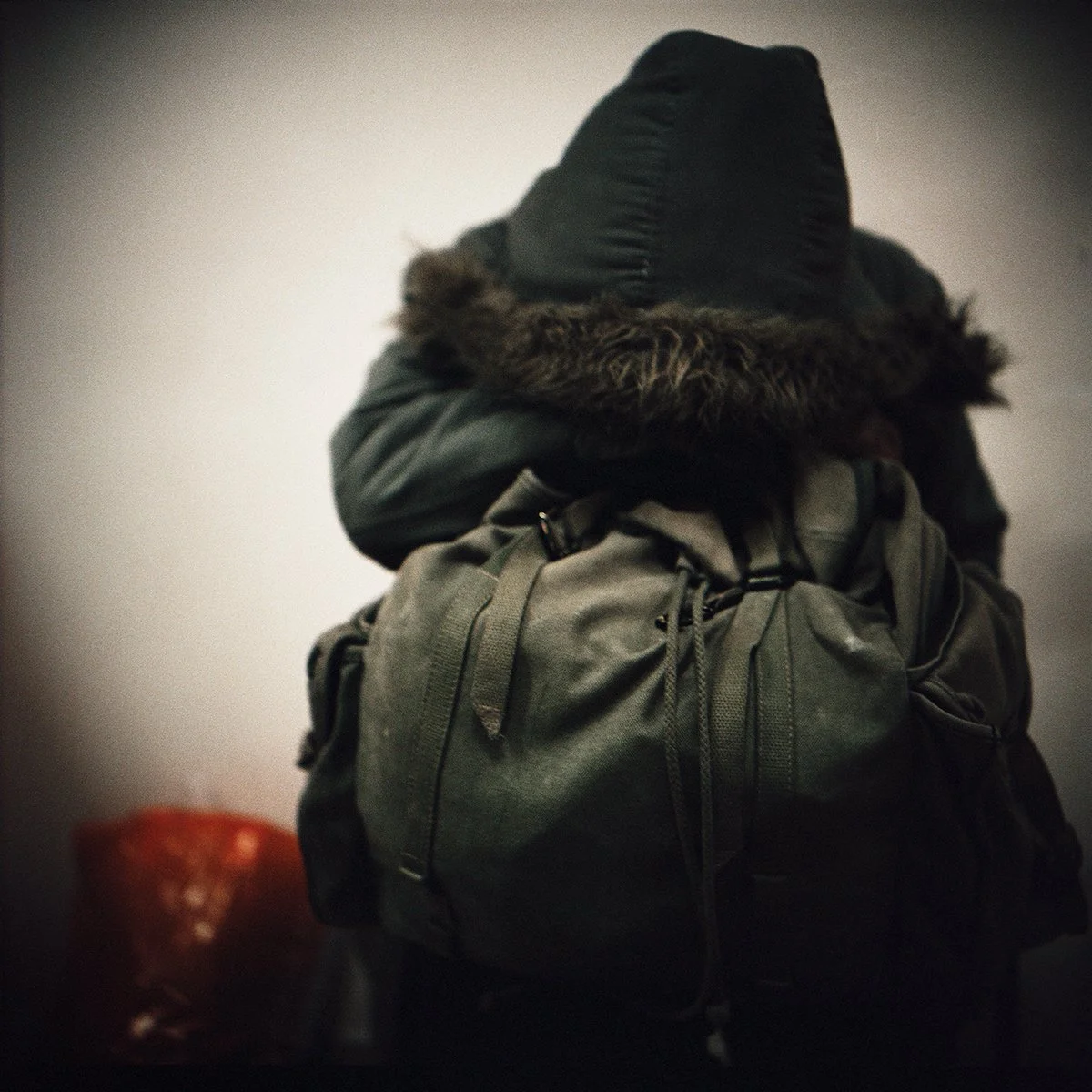 Personne portant une veste à capuche avec une fourrure autour du col, portant un sac à dos, brouillard ou lumière tamisée