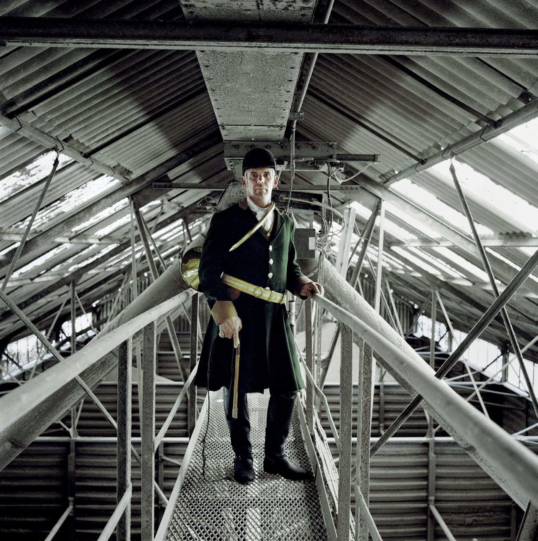 Men in historical uniforms, wearing caps and holding flags, standing on a metal platform in a metal structure.