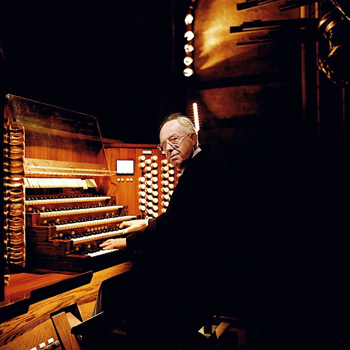 An elderly man plays the organ in a dark room with warm lighting.