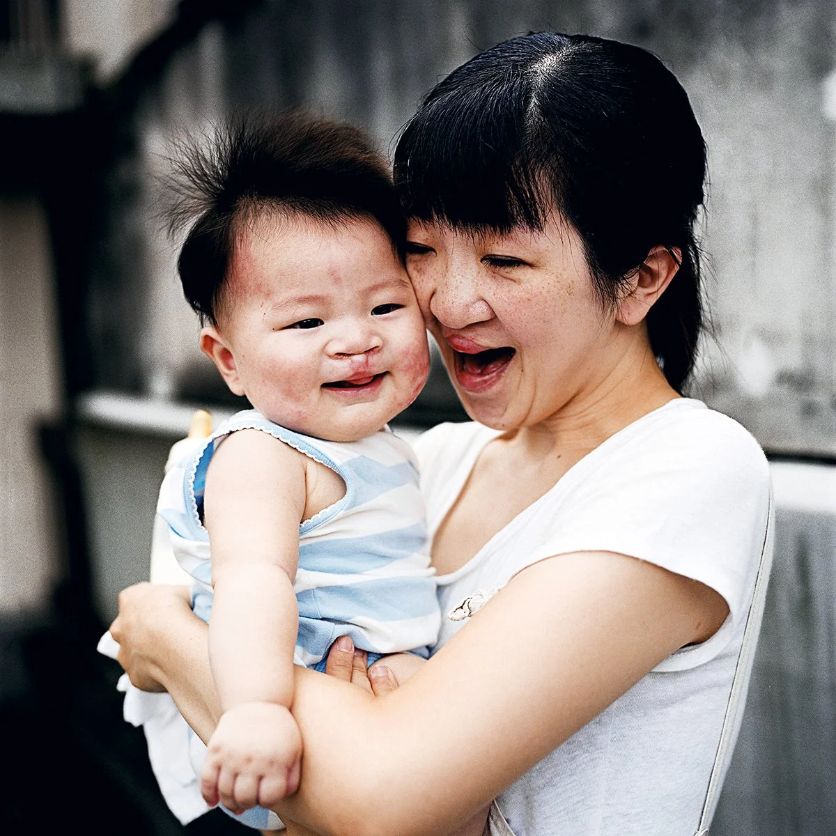 Une femme souriante tient un jeune enfant dans ses bras, tous deux exprimant de la joie.