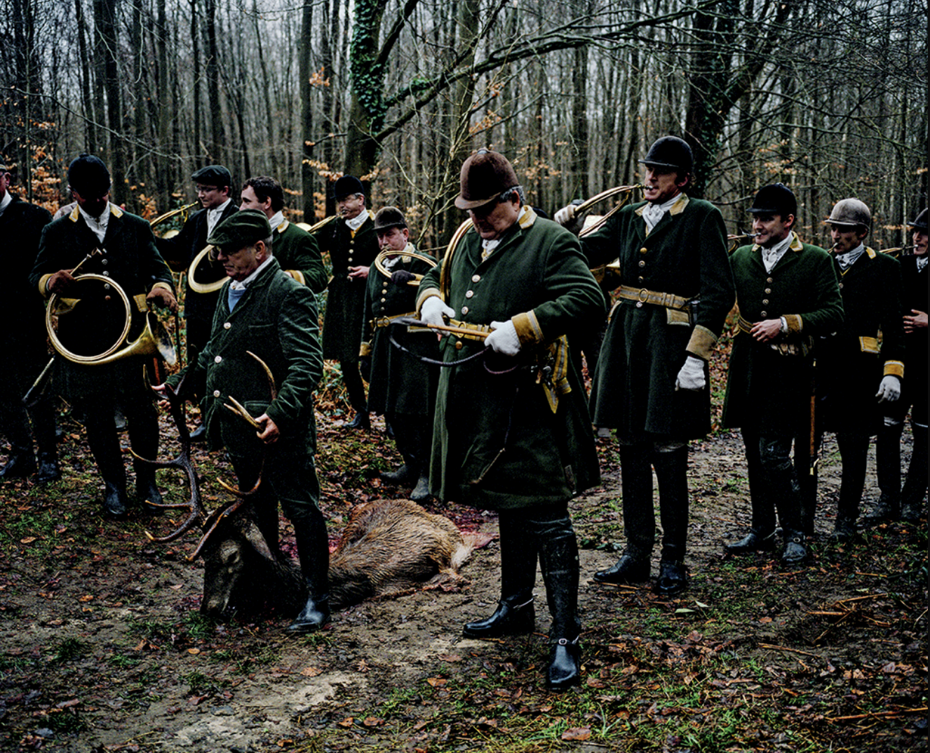 Groupe de chasseurs en forêt, portant des vêtements traditionnels de chasse, avec un sanglier abattu au sol, pendant une chasse au gros game.