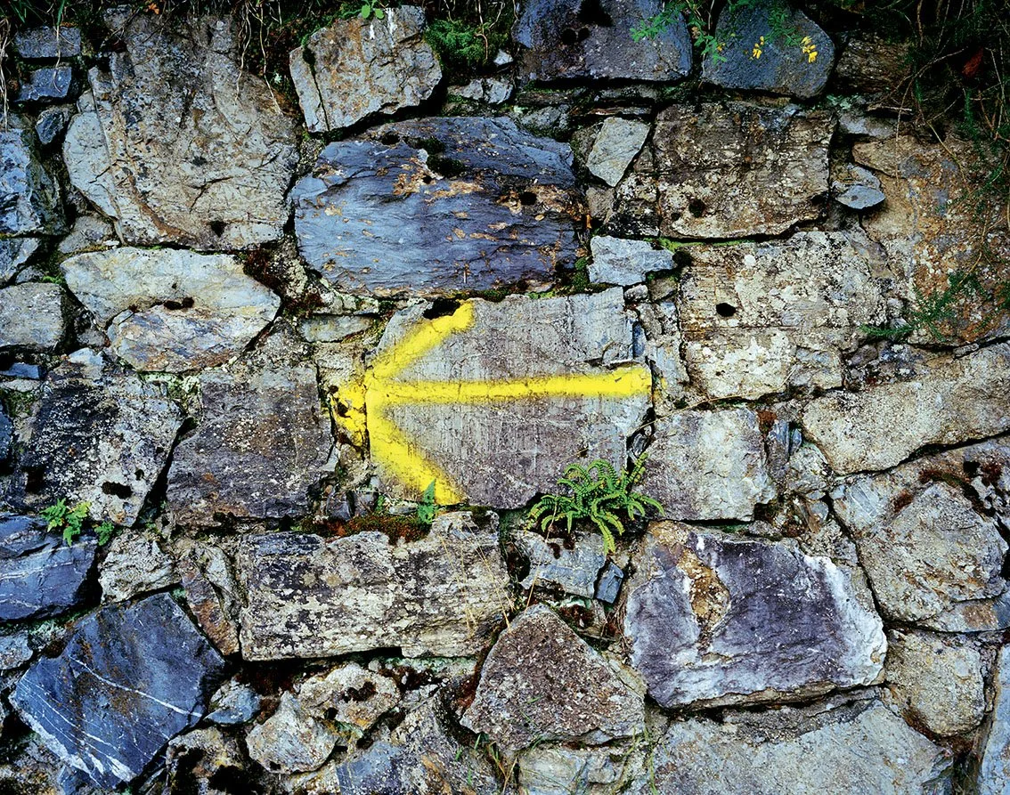 A stone wall with a painted yellow arrow pointing to the left.
