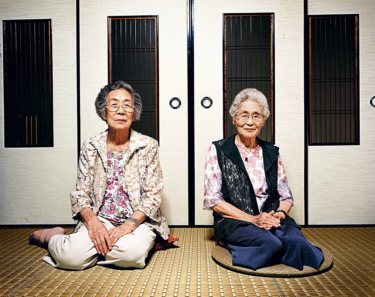 Deux femmes âgées assises sur un tapis japonais devant des portes coulissantes traditionnelles.
