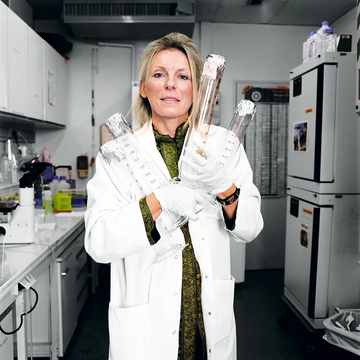 A woman in a lab coat holding several test tubes in a scientific laboratory.
