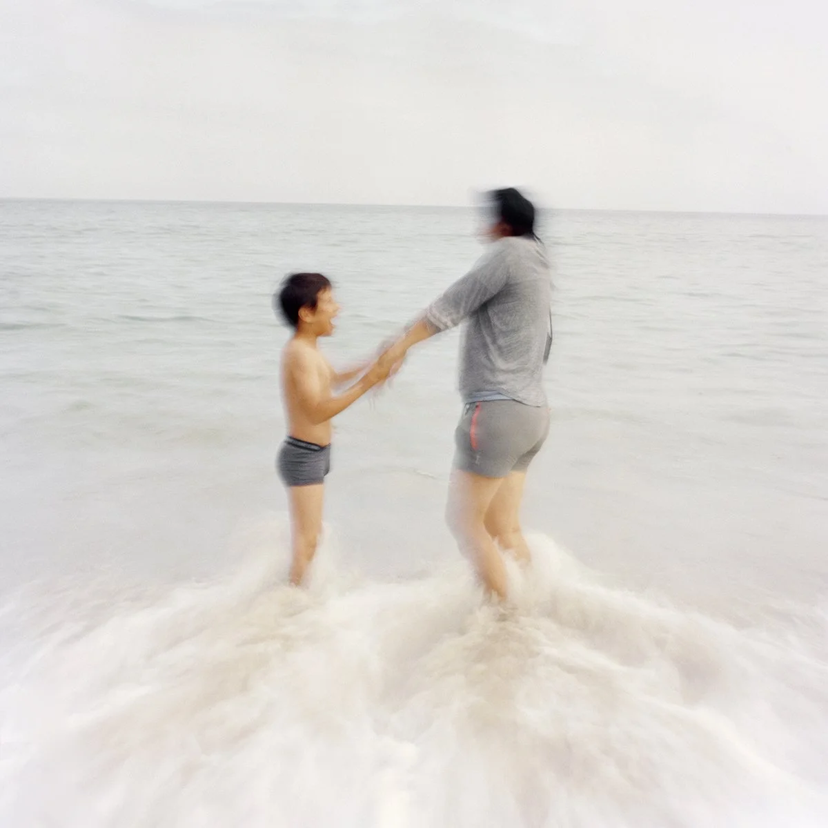 A child and an adult play in the sea water by the beach.