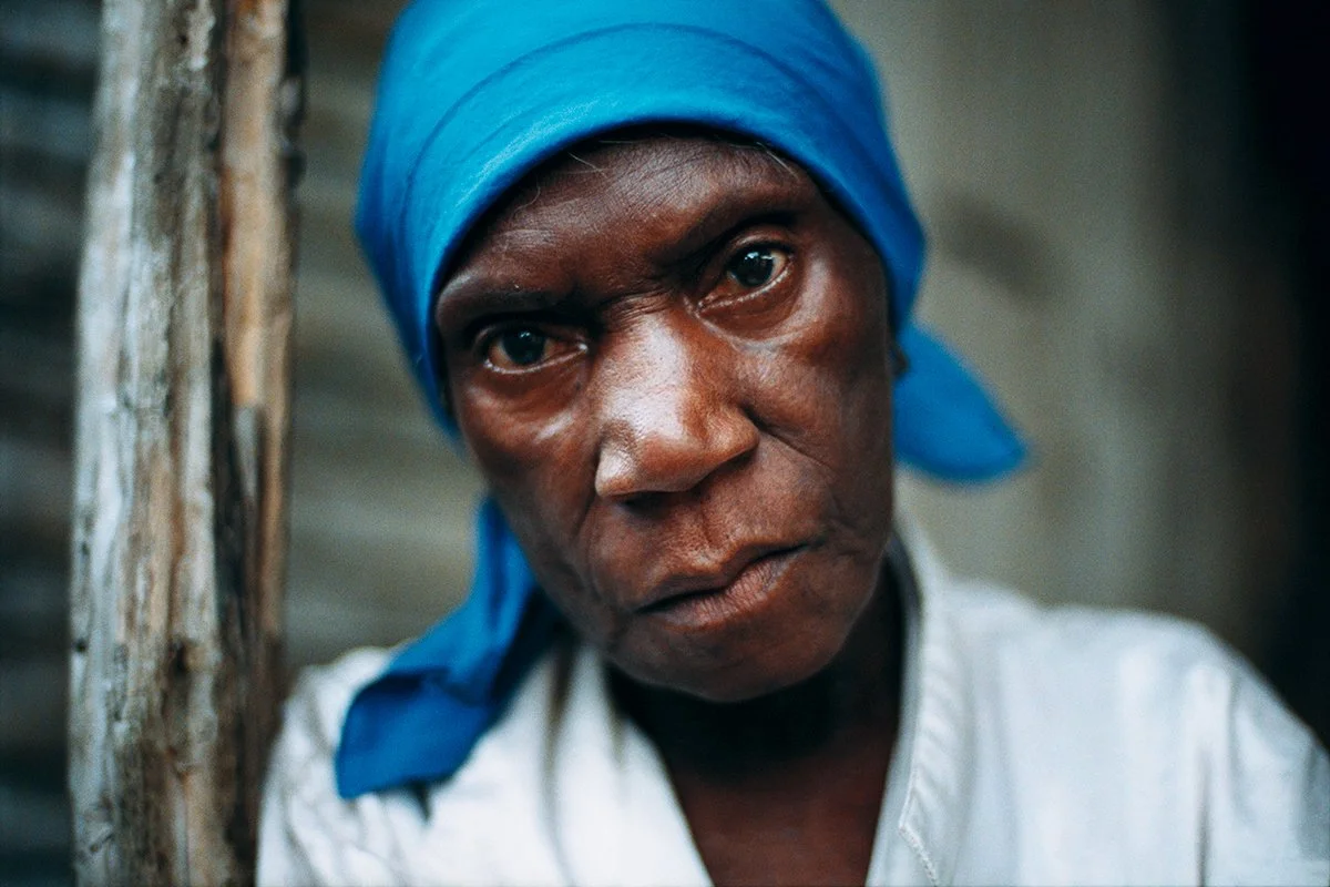 Portrait of an elderly woman wearing a blue scarf, staring into the lens against a blurred background.