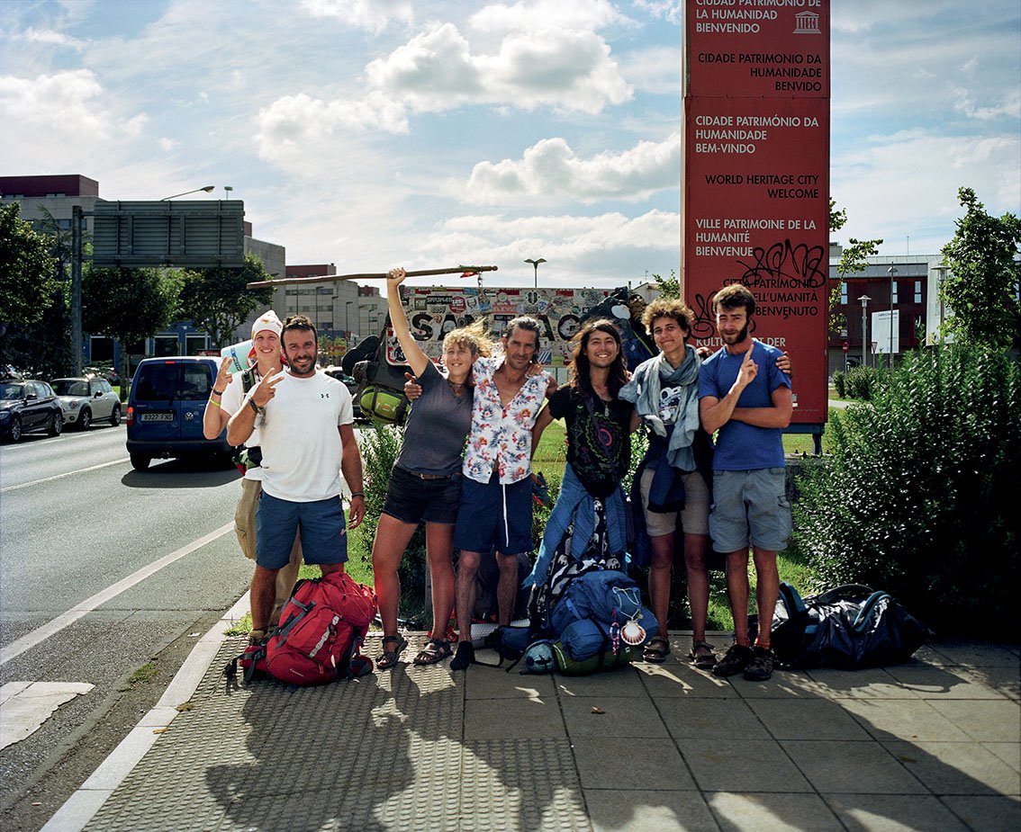 Group of seven people with backpacks, posing in front of a sign indicating that they are in a World Heritage city.