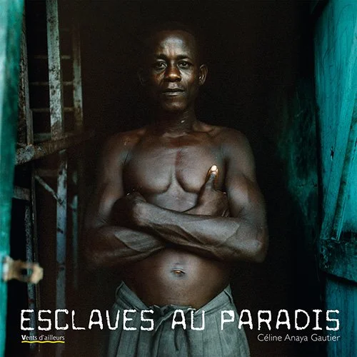 Un homme nu avec les bras croisés dans une pièce sombre, regardant l'objectif, avec le titre "Esclaves au Paradis" en dessous, et le nom Céline Anaya Gautier.