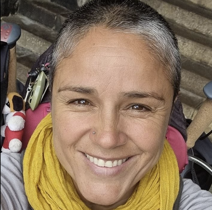 Une femme souriante avec des cheveux courts, portant une écharpe jaune, dans un environnement intérieur.