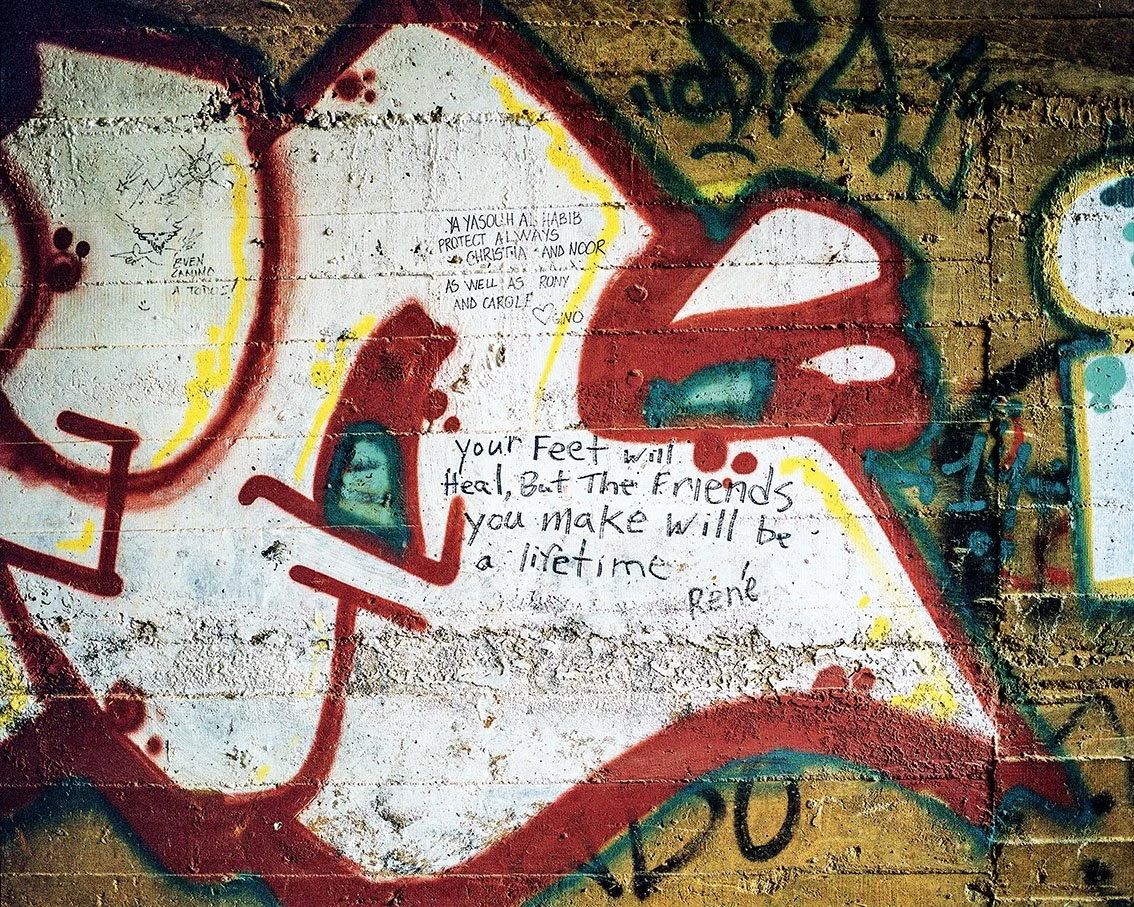 Graffiti on a brick wall with phrases such as "Your feet will heal, but the friends you make will be a lifetime" and colorful drawings.